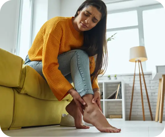 Woman sitting on the floor holding her ankle with visible pain, illustrating symptoms of Achilles tendon rupture such as swelling, tenderness, and weakness in the heel