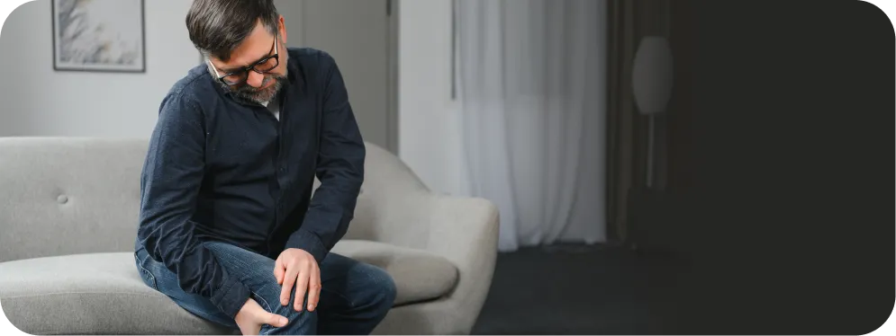 Man sitting on a couch holding his painful knee, showing common symptoms of chronic synovitis and joint inflammation