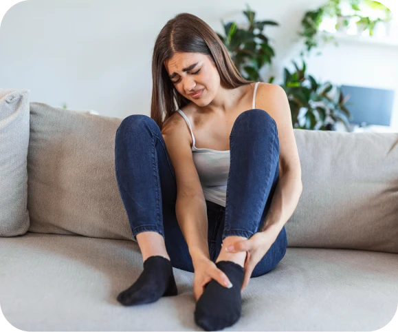 Young woman experiencing ankle pain at home, a common symptom of cartilage injury in the tibiotalar joint.